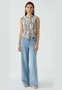 Ärmelloses Oberteil im Schlangenprint mit braunen und beigen Tönen, kombiniert mit hellblauen, weiten Denim-Jeans. Verfügt über ein schwarzes Etikett am Saum.