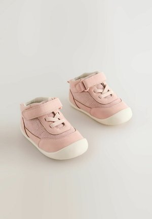 Roze hoge schoenen gemaakt van zacht materiaal met een textuurpaneel, voorzien van een klittenbandsluiting en nep veters, en een witte rubberen zool.