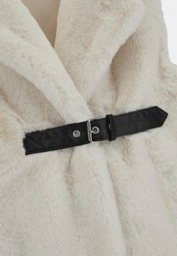 Bontjas in crèmekleur met een zachte textuur, voorzien van een zwarte leren riem en zilverkleurige metalen accenten voor het sluiten.