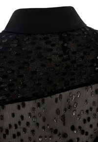 Black top featuring a smooth collar and textured fabric. The fabric includes dotted patterns with varying shapes and a layered design.
