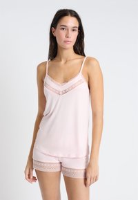 Conjunto de camiseta sin mangas y pantalones cortos de color rosa claro, hecho de una tela suave. La camiseta presenta un detalle de encaje en el escote; los pantalones cortos tienen acentos de encaje en el dobladillo.