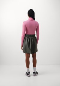 Collo rosato aderente con colletto alto e maniche lunghe; gonna nera in similpelle a vita alta con elastico in vita. Sneakers con calzini bianchi in vista.