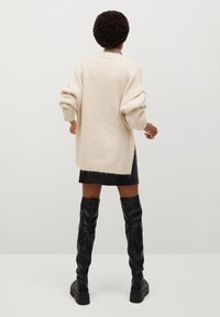 Kremowy, dziany, oversize'owy sweter z opadającymi ramionami, w połączeniu z czarną skórzaną mini spódnicą i wysokimi czarnymi kozaczkami.