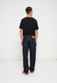 Svart kortermet t-skjorte kombinert med mørkeblå denimjeans med baklommer med dekorative sømmer og en lysebrun lærmerkelapp.