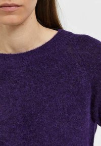 Suéter de punto morado con cuello redondo, superficie texturizada y ajuste ligeramente holgado. El material parece suave y cálido con fibras borrosas.