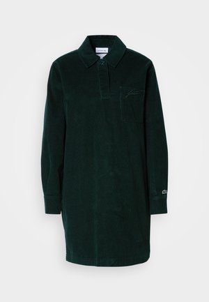 Camicetta in corduroy verde scuro con colletto, taschino sul petto e maniche lunghe. Presenta un dettaglio del logo sulla manica.