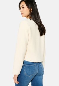 Crème-kleurige cropped trui van een gestructureerde stof, met een ronde halslijn en lange mouwen, gecombineerd met blauwe jeans. Fluffy, zachte stof.