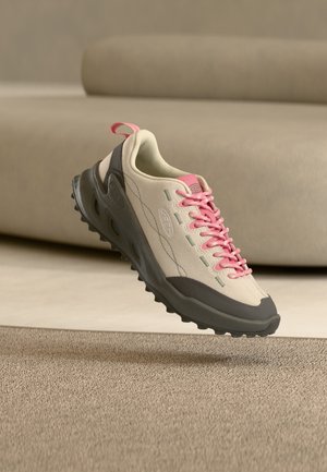 Helebeež ja hall toss roosade paeltega, mis ripub beeži vaiba kohal neutraalse tooniga ruumis, mille taustal on diivan.