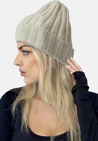 Light beige knitted beanie with a ribbed pattern and a folded brim, displaying a soft texture and relaxed fit.