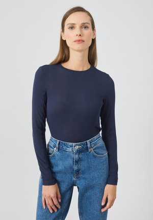 Marineblå langermet topp med rund hals, laget av et glatt, elastisk materiale, kombinert med høy midje blå denimjeans.