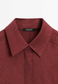 Col de chemise bordeaux à manches longues avec bouton et étiquette "Massimo Dutti Made in China", tissu texturé, col plié.