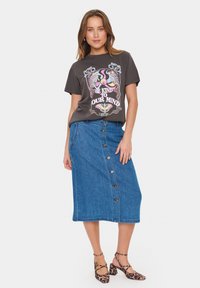 Temno siva grafična majica s pisanem dizajnom, v kombinaciji z modrim denim midi krilom z gumbi spredaj. Čevlji z blok peto v leopardjem vzorcu.