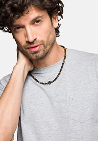 Szara koszulka z kieszonką z przodu, połączona z naszyjnikiem z koralików, zawierającym czarne i brązowe kamienie, wzbogaconym okrągłym czarnym akcentem.