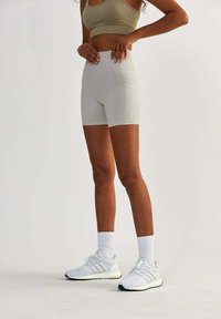 Shorts actifs gris clair en tissu extensible, dotés d'une taille haute et de deux poches latérales, associés à des chaussures de sport blanches et des chaussettes.