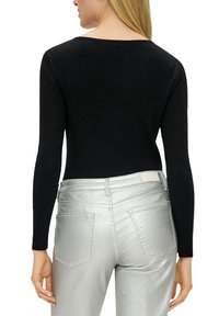 Zwarte geribbelde top met lange mouwen en een V-vormig detail aan de achterkant, gecombineerd met glanzende zilveren skinny jeans met achterzakken en een soepele textuur.