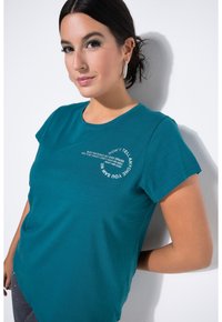 Teal, T-shirt met korte mouwen, gemaakt van katoen en met een ronde hals. Voorzien van witte tekst in een gebogen lay-out: "VERTEL HET NIEMAND...".