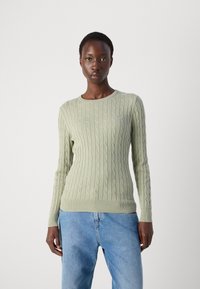 Maglione a coste verde chiaro con maniche lunghe, scollo rotondo e orlo a coste. Abbinato a jeans blu, con un piccolo dettaglio del logo.