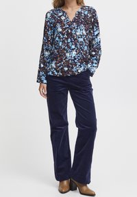 Blusa floreale in blu e marrone su pantaloni navy, con scollo a V, maniche lunghe e vestibilità ampia. Pantaloni in corduroy testurizzato.