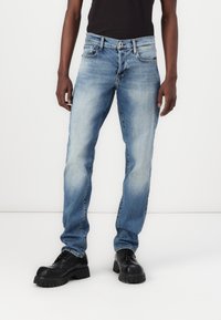 Lichtblauwe denimjeans met een rechte pasvorm, vervaagde delen, vijf zakken en een zwart t-shirt, gecombineerd met stevige zwarte schoenen.