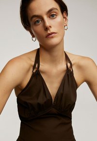 Top marrón con cuello halter hecho de una tela suave, con un detalle de pechera fruncida. Presenta tirantes finos y un diseño simple y limpio.