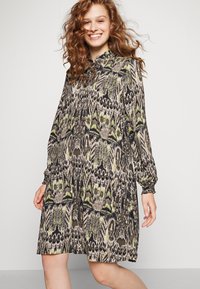 Robe à manches longues, longueur genou, en tissu à motifs avec des tons noirs, verts et beiges, à coupe décontractée et col à bouton.