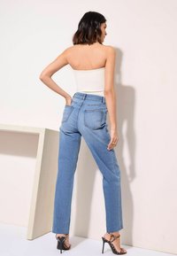 Heledad sinise värvi kõrge vöökohtadega teksad otse säärega, millel on tagataskud ja õrn tuhmumine, koos sobiva valge topi ja mustade kontsadega.