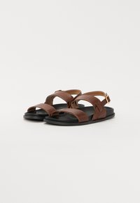 Sandalias de cuero marrón con suela negra, con correas cruzadas y hebilla ajustable, diseño de punta abierta, textura suave.