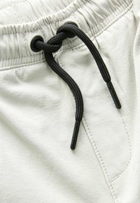 Shorts gris clair avec une taille élastique et un cordon de serrage noir. Texture lisse avec un motif subtil et des détails de couture renforcée.