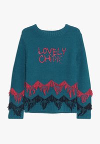 Maglione lavorato a maglia color teal con la scritta "LOVELY CHIPIE" in lettere rosse, con accenti frangiati rossi e neri sull'orlo e sulle maniche.