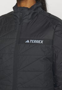 Giacca trapuntata nera con collo alto e zip frontale. Presenta un logo TERREX e un tessuto testurizzato con cuciture diagonali. Design leggero.