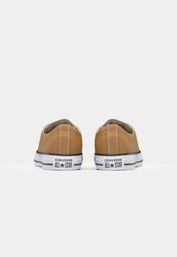 Taanse canvas lage sneakers met witte rubberen zolen, zwarte strepen en het "Converse All Star" logo op de hak. Zichtbare stikdetails.
