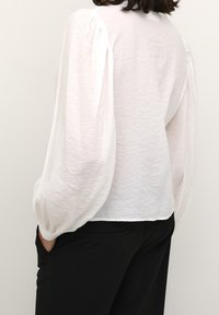 White textured blouse with puffed long sleeves, paired with black pants. Blouse features a slightly relaxed fit and rounded hem.