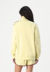 Yellow fleece sweatshirt with a high collar and ribbed hem. Features contrasting accents on shoulders and cuffs. Smooth texture.
