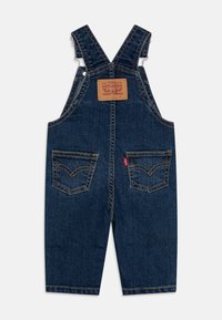 Džínové lacláče tmavě modré barvy s nastavitelnými ramínky, koženou záplatou na zádech a dvěma předními kapsami s kontrastním prošíváním.