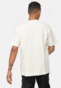 Creme bomulds t-shirt med korte ærmer i afslappet pasform og rund hals, med en tekstureret overflade og synlige sømme.