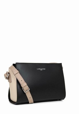 Sac à main en cuir noir et beige avec un design rectangulaire, une bandoulière ajustable et un logo en relief sur le devant. Texture lisse.