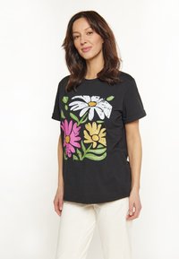 Sort bomulds T-shirt med et blomstermotiv i hvid, pink og gul med grønne blade. Kortærmet, afslappet pasform.