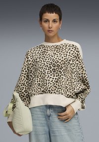 Sweatshirt à motifs léopard en beige et marron avec une coupe décontractée, col rond et poignets côtelés. Associé à un sac pochette vert clair et un jean bleu.