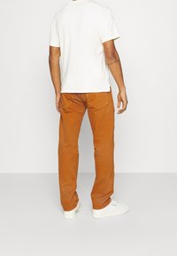 Orangen Baumwollhosen mit geradem Bein, ausgestattet mit zwei Gesäßtaschen, kombiniert mit einem weißen T-Shirt mit kurzen Ärmeln und weißen Sneakers.