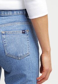 Ljusblå denimjeans har en diamantformad bakficka med en liten, mörkblå etikett. Jeansen har en klassisk passform och en mjuk textur.