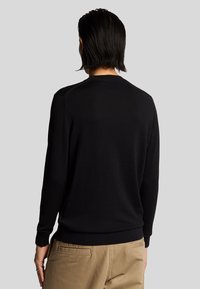 Maglione nero a maglia con maniche lunghe, scollo tondo, polsini e orlo a coste. Texture liscia con design minimale.