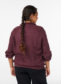 Gestrickter Pullover in tiefem Burgunderrot mit strukturiertem Rippenmuster, weiten Ärmeln und lockerem Sitz, kombiniert mit schwarzer Hose.