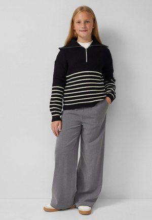 Zwart-wit gestreepte gebreide trui met een kraag en rits, gecombineerd met grijze wijde broek en witte schoenen.