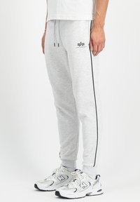 Sive bombažne trenirke s črnimi stranskimi črtami, elastičnim pasom in logotipom. V kombinaciji z belimi in sivimi športnimi čevlji.