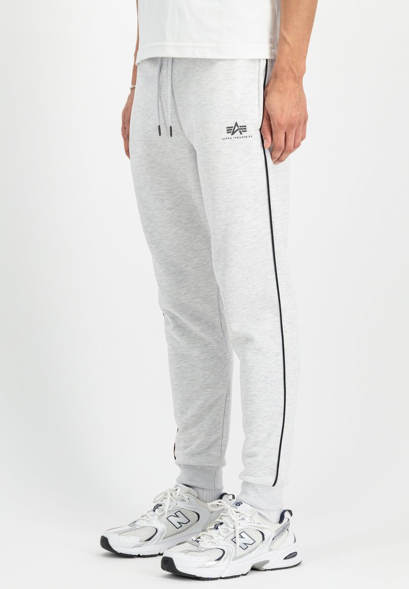 Sive bombažne trenirke s črnimi stranskimi črtami, elastičnim pasom in logotipom. V kombinaciji z belimi in sivimi športnimi čevlji.