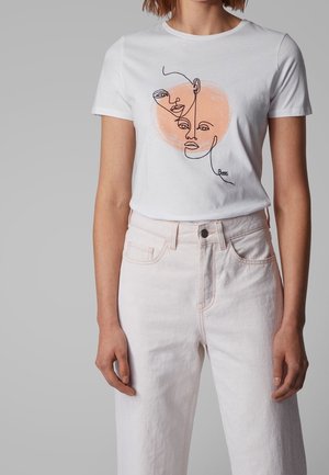 Biała bawełniana koszulka z minimalistycznym rysunkiem twarzy w czerni z brzoskwiniowym okrągłym akcentem. Do tego jasnoróżowe, wysokie spodnie jeansowe.