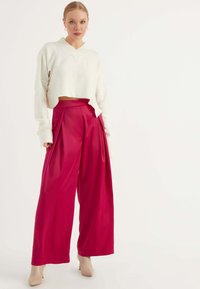 Witte cropped sweater met een v-hals en lange mouwen, gecombineerd met hoogbare, wijde roze broek met plooien. Lichtbeige hakken.