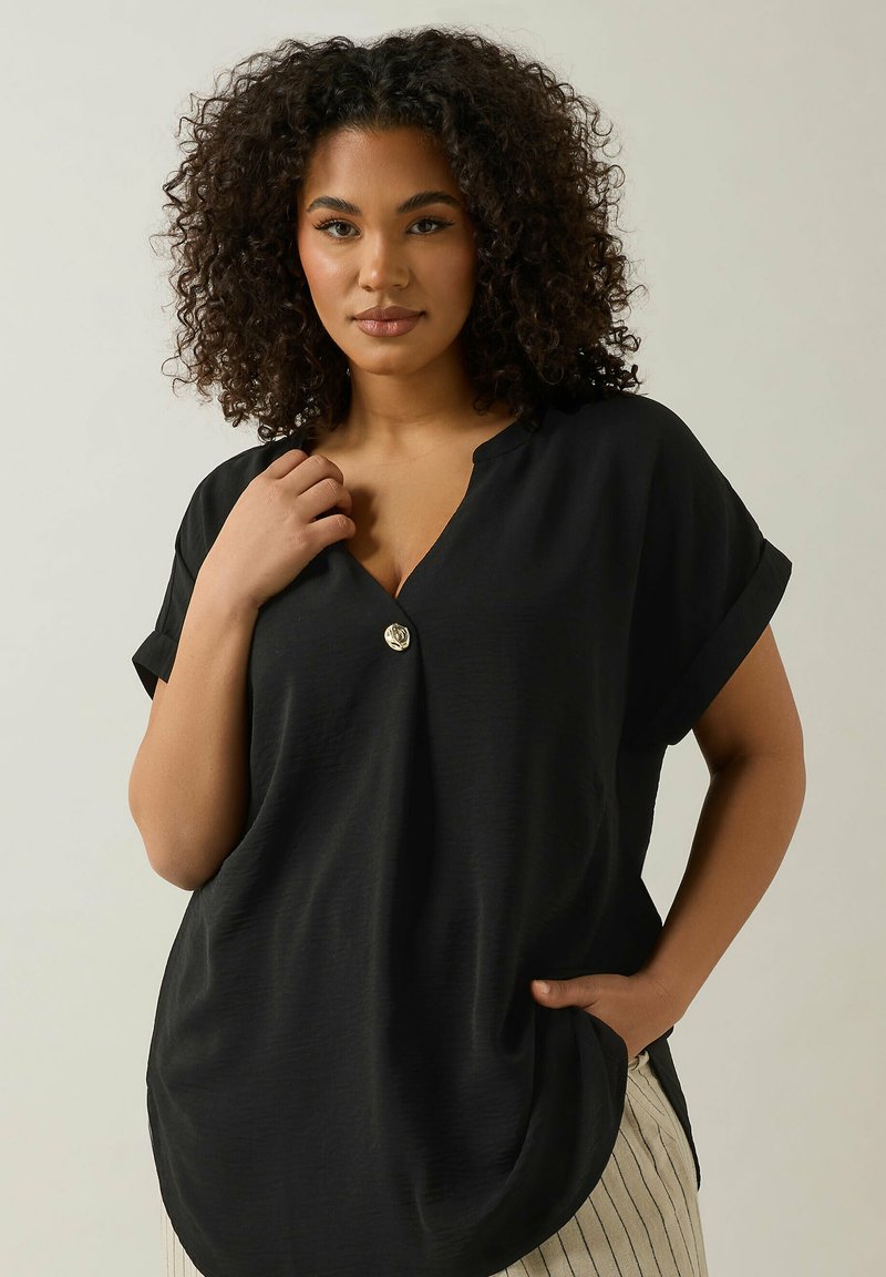 Blusa nera con un fit rilassato, maniche corte arrotolate, scollatura a V e un bottone decorativo al colletto. Tessuto liscio e forma drappeggiata.
