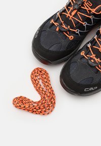 Svarte sportsko med oransje snørebånd og akenter, med teksturert stoff og gummisåler. Inkluderer et separat flettet oransje snørebånd.
