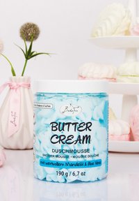 Container of turquoise shower mousse labeled "Butter Cream" with white lid. Contains almond oil and aloe vera, 190g. Textured whipped cream design.